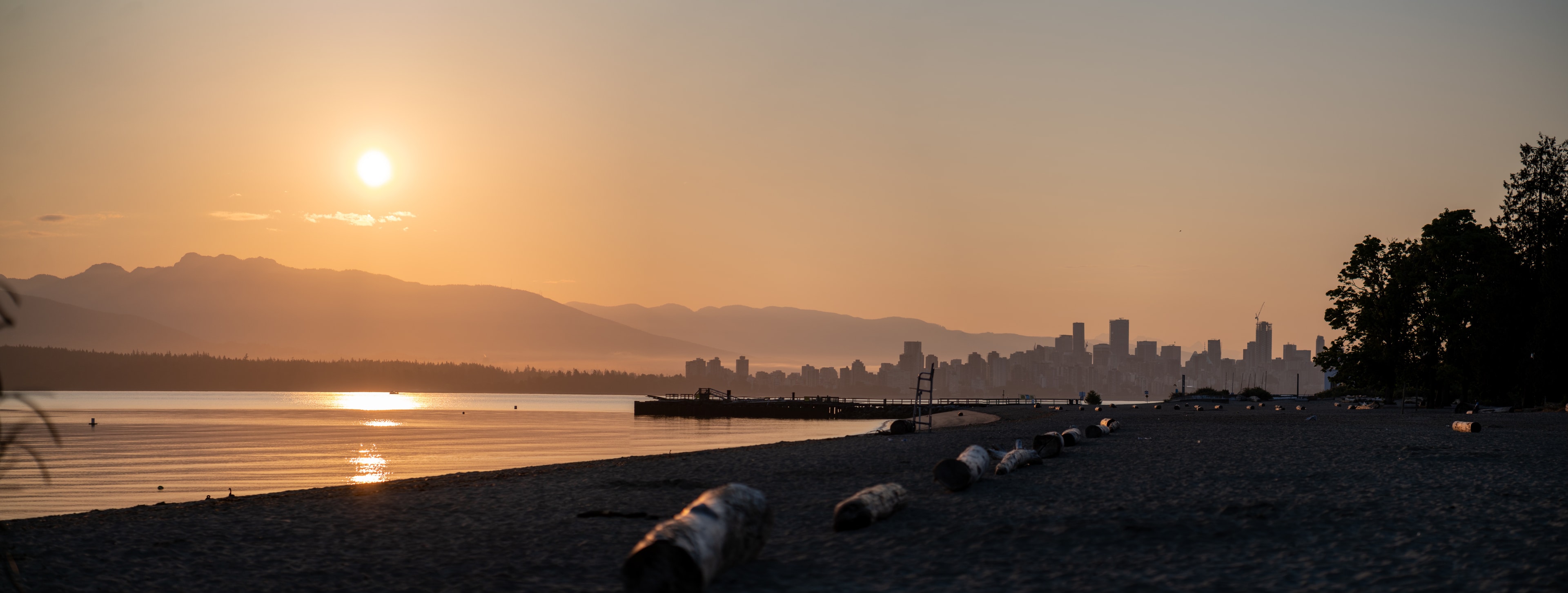 A beach at sunset with mountains and a city skyline in the distance.
