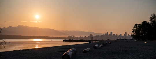 A beach at sunset with mountains and a city skyline in the distance.