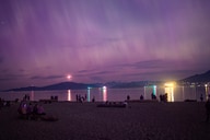 A nighttime beach scene under a purple sky, with people silhouetted against reflected light on the water.