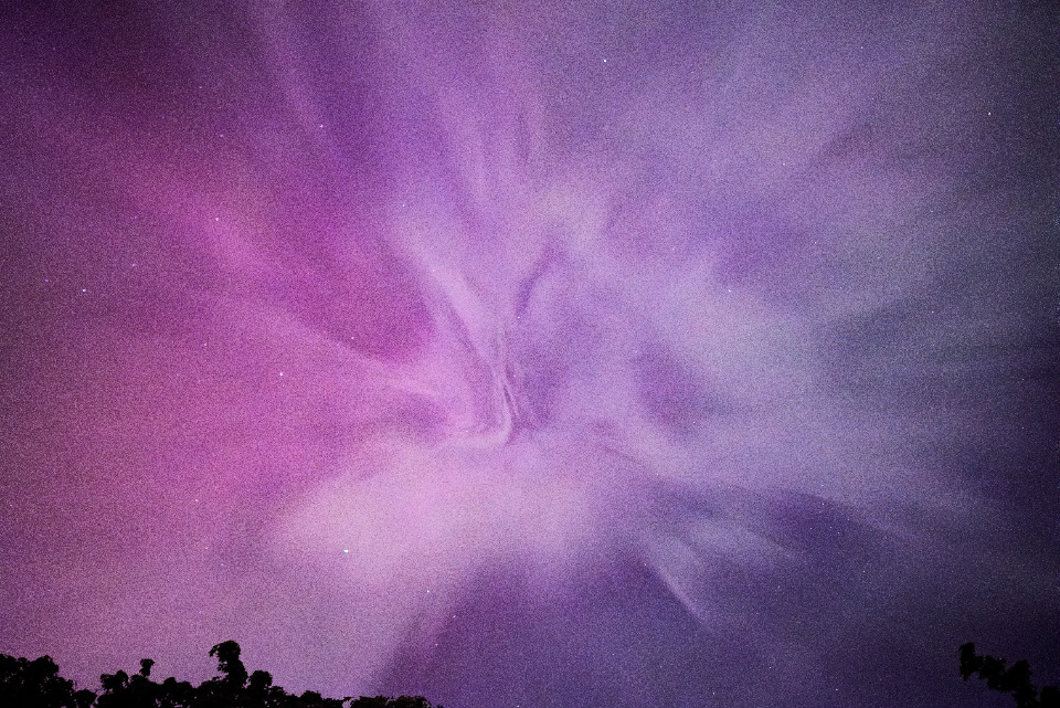 A vivid, ethereal capture of a night sky. The image showcases swirling clouds and distant stars set against a mesmerizing palette of purple and pink.