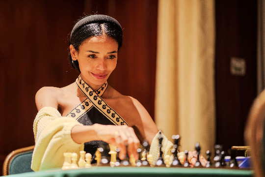 A woman studies a chessboard, face lit by the table in front of her.