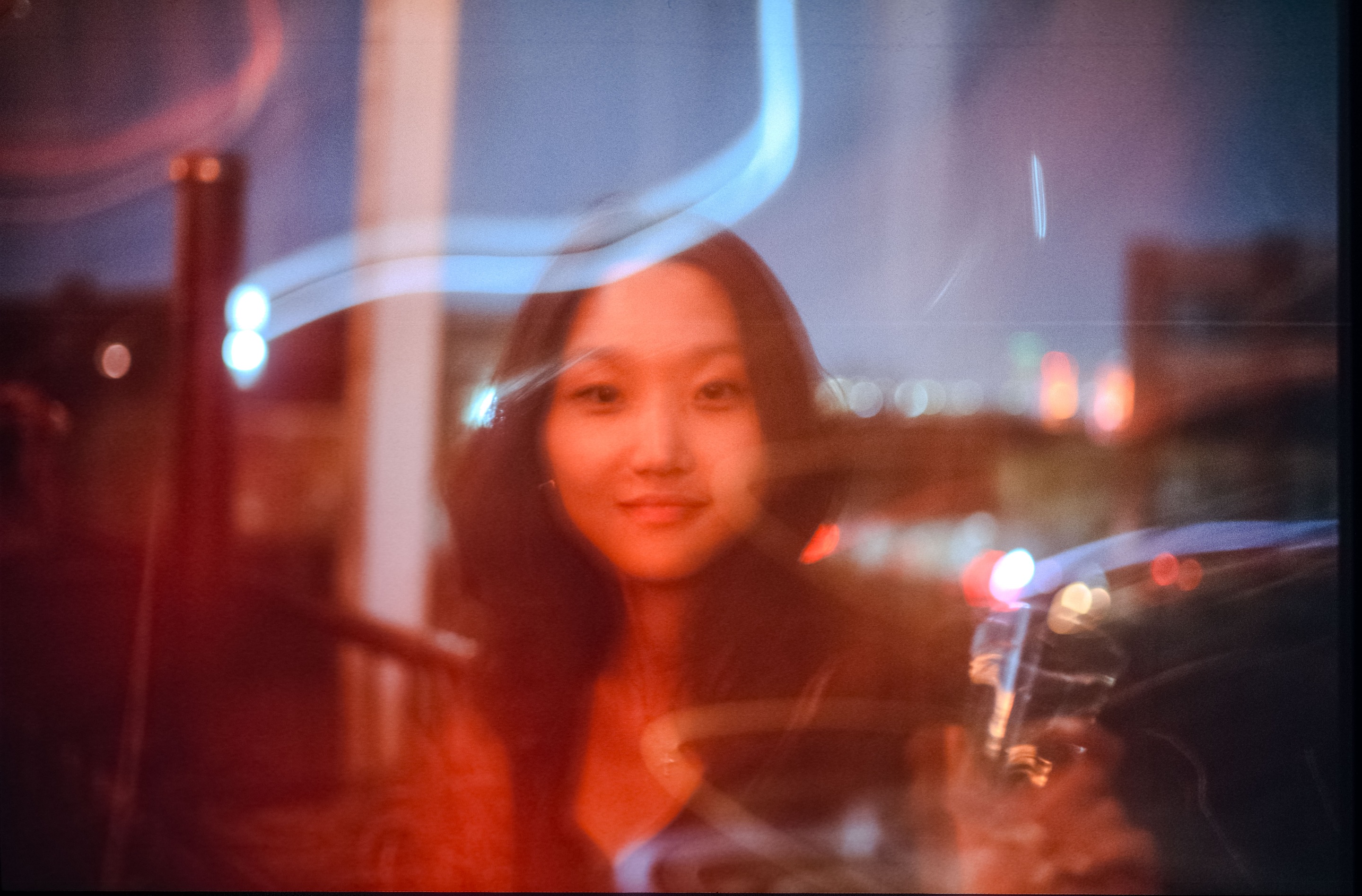 A soft, dreamlike portrait of a young woman, with streaks of light and blurred city lights in the background.