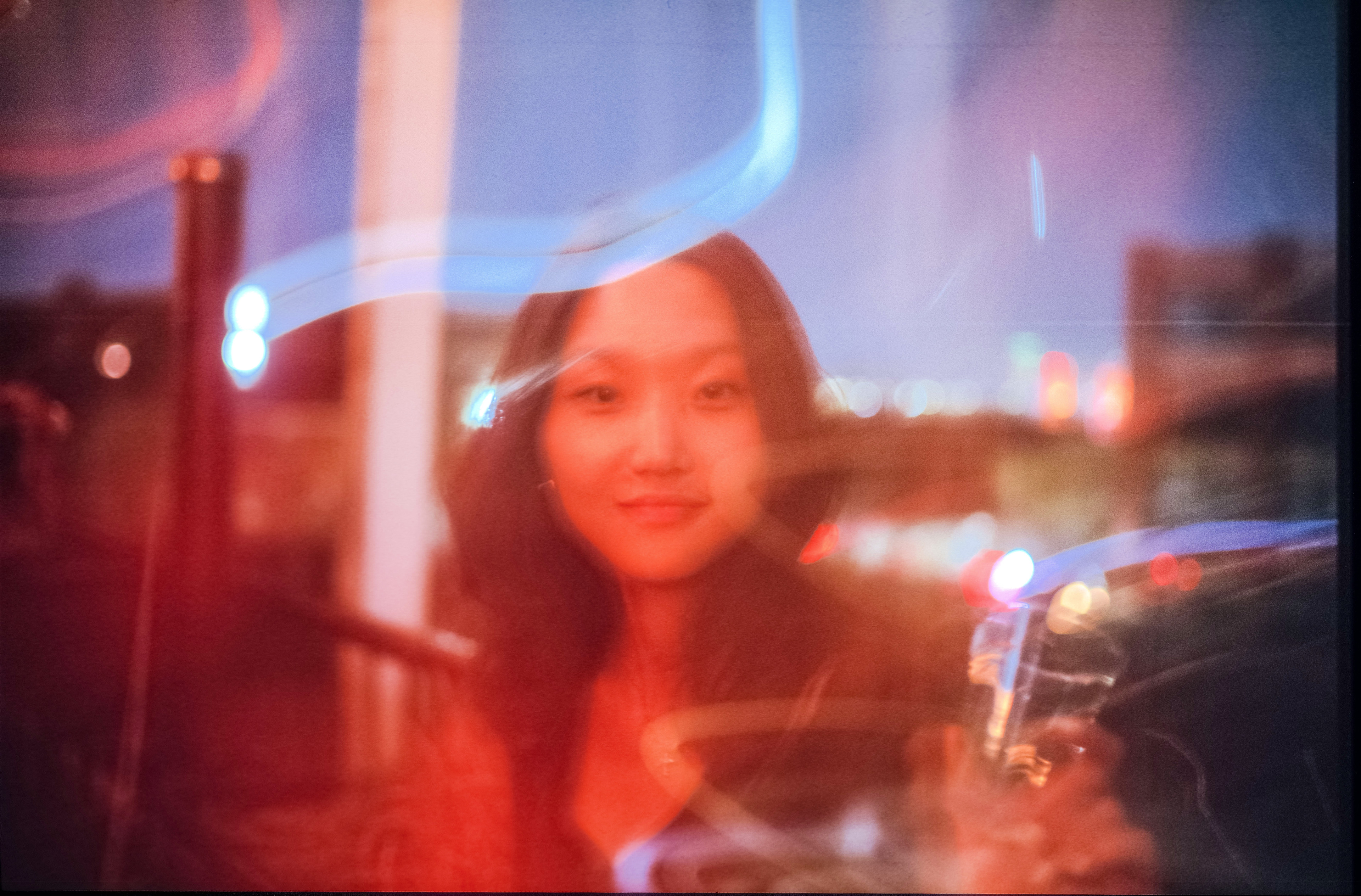 A soft, dreamlike portrait of a young woman, with streaks of light and blurred city lights in the background.
