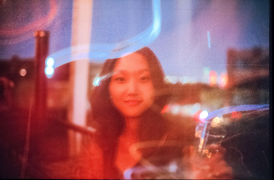 A soft, dreamlike portrait of a young woman, with streaks of light and blurred city lights in the background.