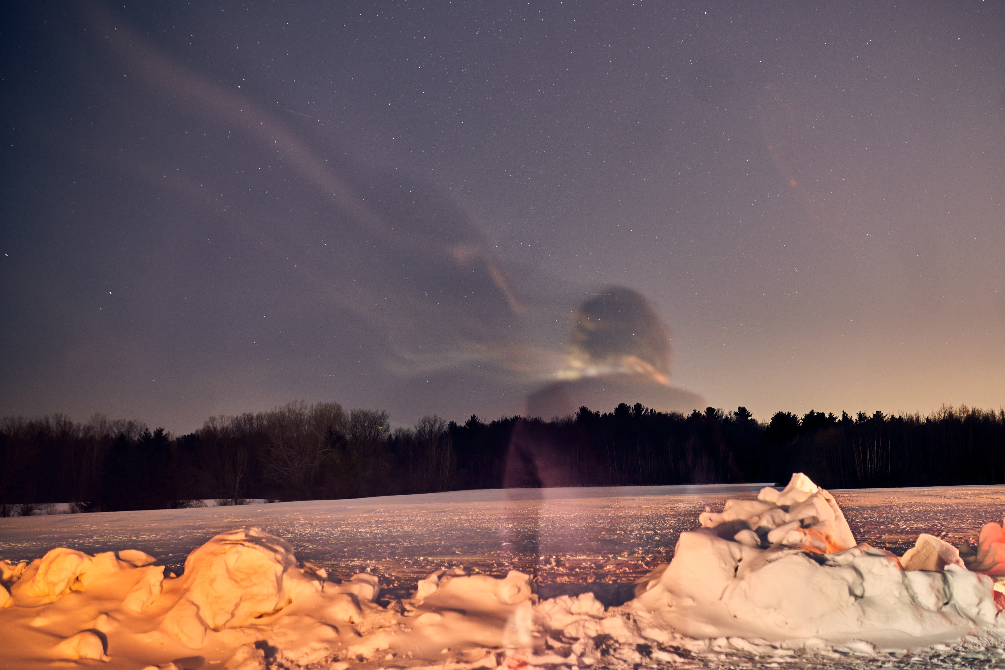 A snowy field with dark trees under a starry sky. A pale form sits in the middle distance.
