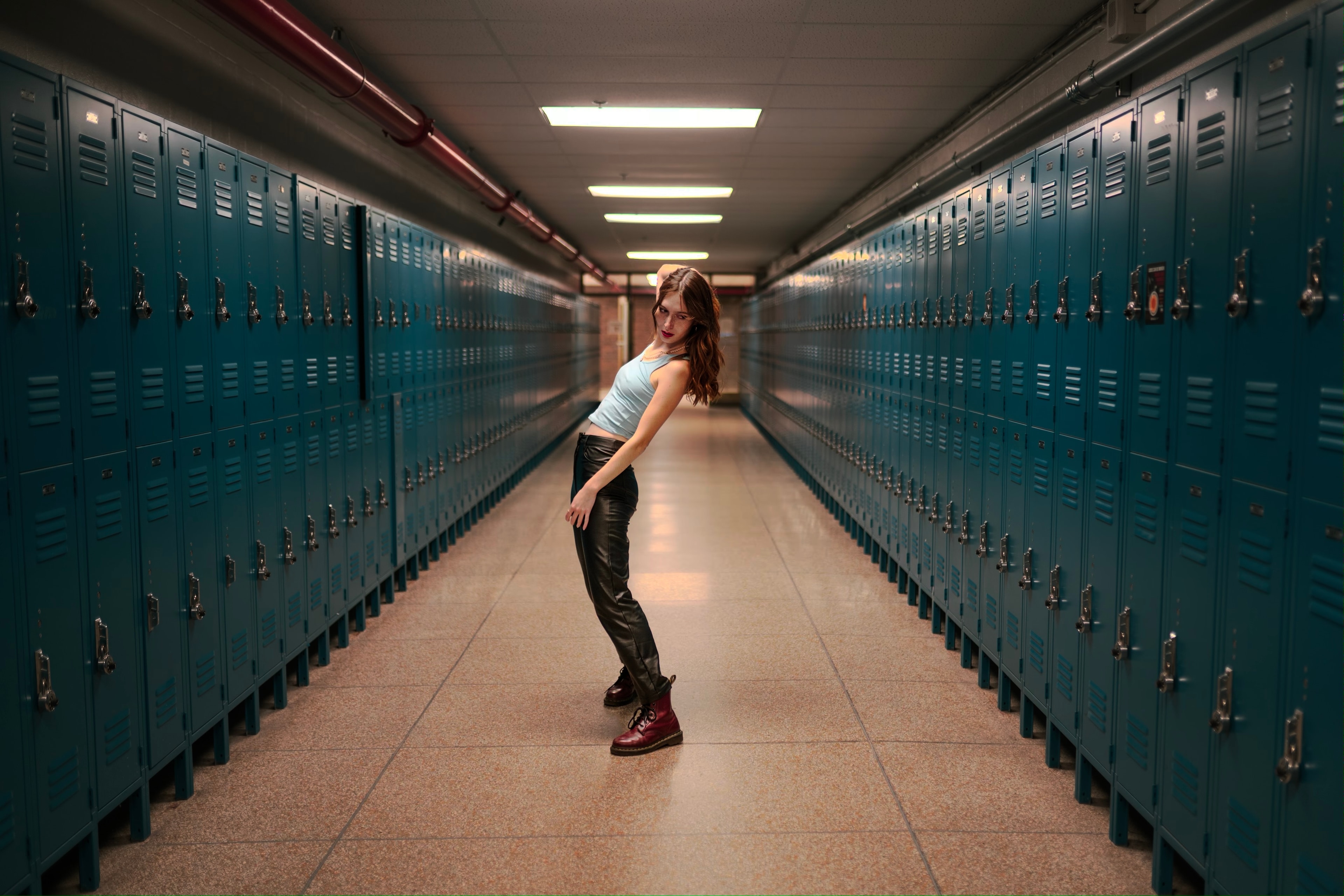 A woman poses in a school hallway lined with teal lockers.