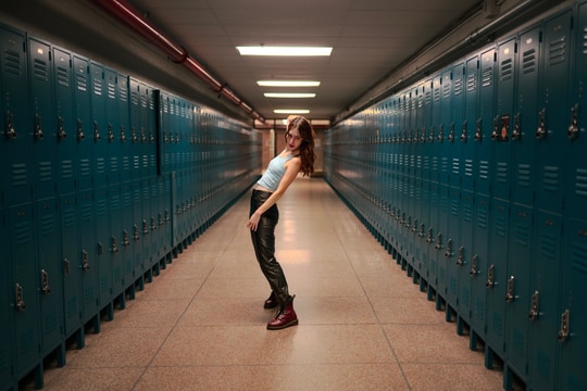 A woman poses in a school hallway lined with teal lockers.